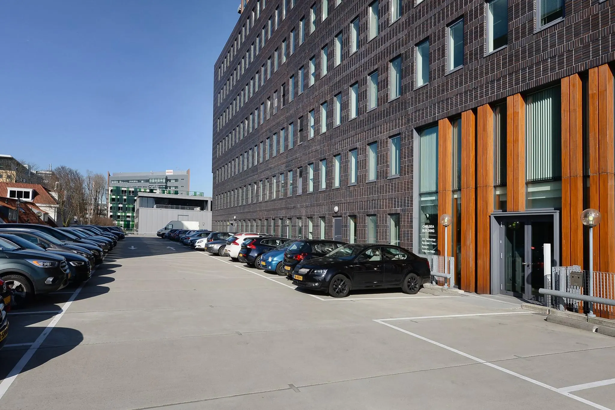 Parkeerterrein naast het Chelsea Building aan de Laan van Zuid Hoorn met geparkeerde auto's en moderne kantoorgebouwen.
